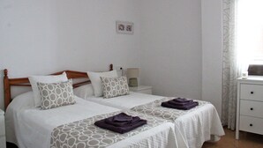 A double bed with a wooden headboard, two bedside tables, a nightstand, a lamp, and a window with patterned curtains. - 1 Bed 1 Bath Luxurious Apt Villamartin Plaza, Golf, Fun & Sun (Orihuela Costa)