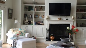 Ein großzügiges Wohnzimmer mit Kamin, weißen Möbeln und einem flachbildfernseher, der darüber angebracht ist.