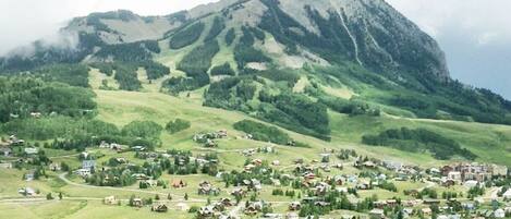 A rural village with houses spread across a green valley, surrounded by hills and a prominent mountain in the background.