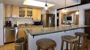 Een moderne keuken met houten kastjes, roestvrijstalen apparatuur en een bar met krukken.