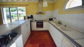 Une cuisine avec des meubles blancs, un four à micro-ondes, un évier et une fenêtre donnant sur l’extérieur.