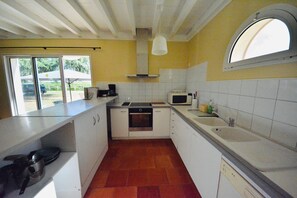 Une cuisine avec des meubles blancs, un four à micro-ondes, un évier et une fenêtre donnant sur l’extérieur.