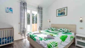 A bedroom with a bed, a crib, a window with curtains, a wall-mounted light, and a framed picture. - Amazing home in Pula with WiFi (Pula)