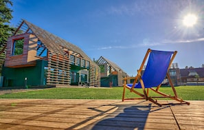 A modern building with a sloped roof, a wooden deck, and a blue beach chair.