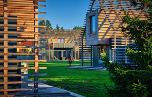 A modern building with a wooden facade, a small tower-like structure, and a grassy courtyard.
