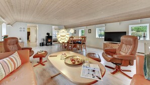 Un vaste salon doté d’un grand plafond en bois, un coin repas avec une table ronde et des chaises, un téléviseur et une cheminée.