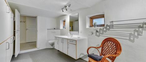 A bathroom with a white sink, mirror, and toilet. There is a wicker chair with a towel on it.