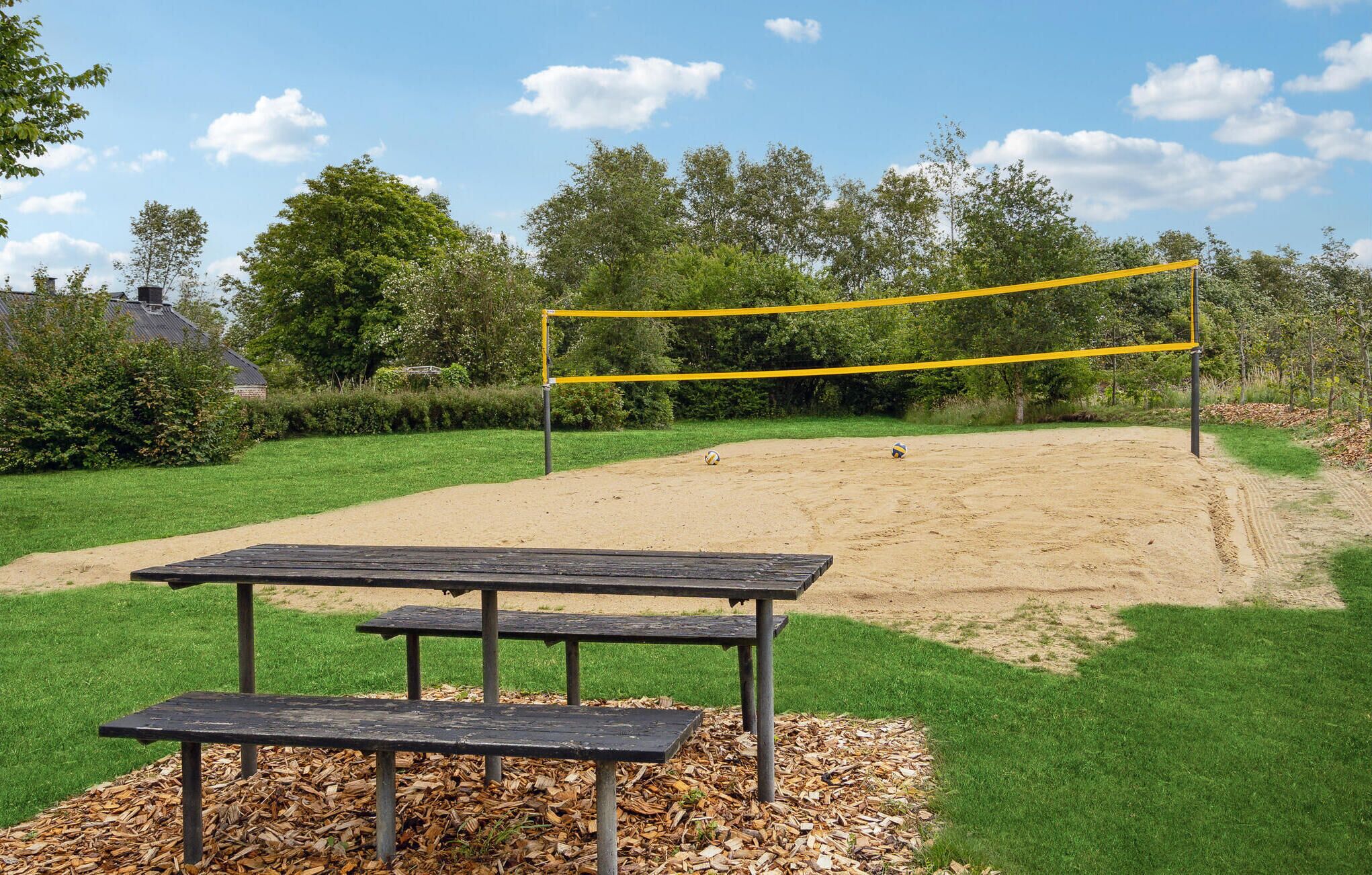 Een volleybalnet in een zandveld, met een picknicktafel op de voorgrond.