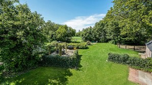 Un jardin bien entretenu, avec un chemin bien défini, un espace barbecue et un mur en briques d’un côté.