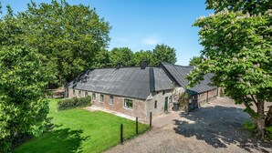 Un bâtiment en briques de deux étages, doté d’un toit en pente, entouré d’une végétation luxuriante et accessible par une allée gravillonnée.