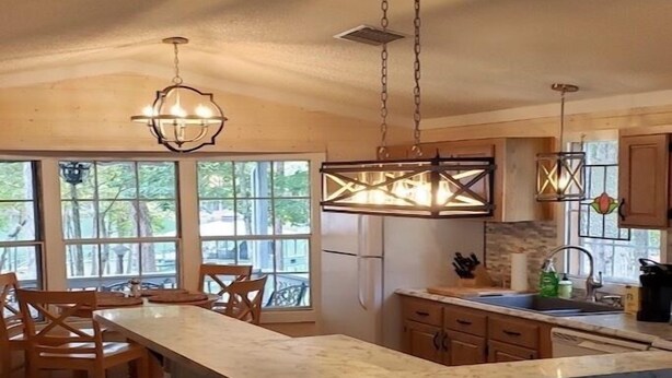 A kitchen with a large island, wooden chairs, hanging pendant lights, and large windows.