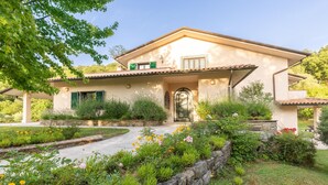 Uma casa em estilo mediterrâneo com telhado de telhas, caminho de pedra e diversos plantas floridas no jardim.