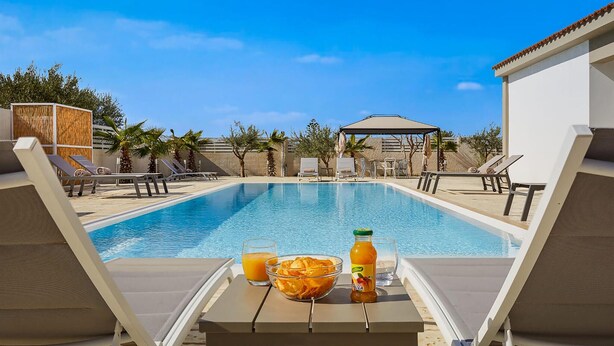 Zona de piscina con sillas de descanso, un área de estar cubierta, una botella de jugo y un bol de papas fritas.