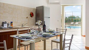Una cocina moderna con horno integrado, un comedor con mesa de vidrio y vistas a una piscina.