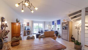 A spacious living area with a wooden dining table, comfortable seating, and a television in the background. - 4 bedroom gorgeous home in Wemeldinge (Wemeldinge)