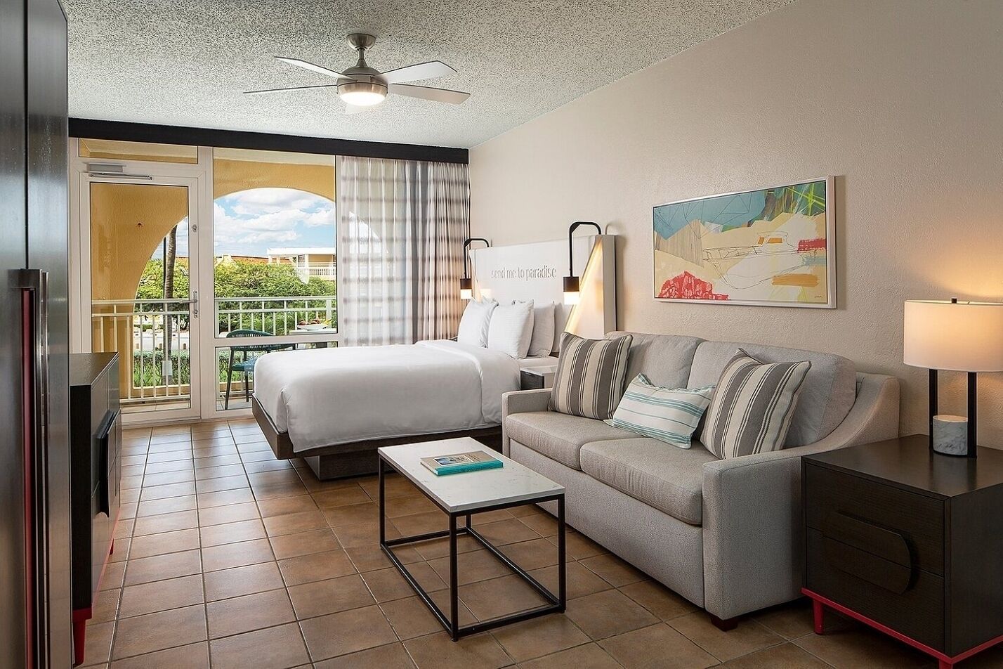 A hotel room with a bed, a sofa, a coffee table, a desk, and a balcony with a view.
