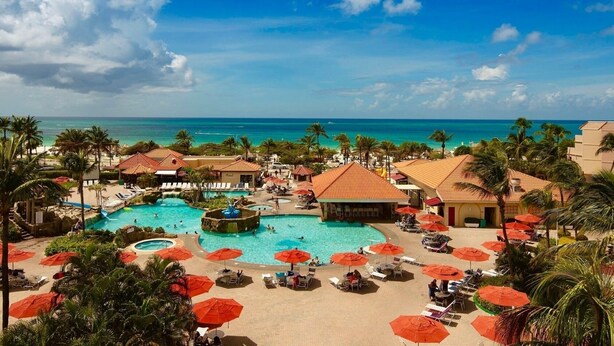 A resort with multiple swimming pools, palm trees, and beach umbrellas.