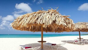 A beach with thatched umbrellas and white lounge chairs.