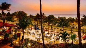 A beachfront restaurant with outdoor seating, palm trees, and a view of the ocean at sunset.