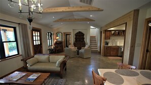 Un ampio soggiorno con soffitto in legno, una zona pranzo con un tavolo grande e una cucina visibile attraverso un'apertura.