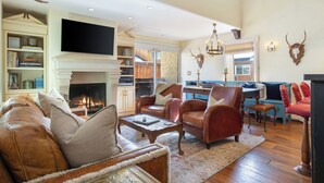 A spacious living room with leather sofas, a fireplace, a television, and a dining area with a blue sofa and red chairs.