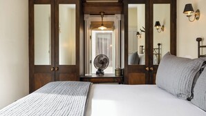 A bedroom with a large bed, wooden wardrobe, a bedside table with a fan, and wall-mounted lamps.