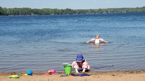 Une scène de plage où un enfant joue dans le sable et un autre nage dans l’eau.