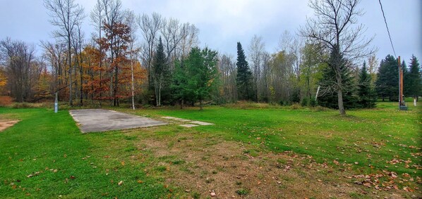 A grassy area with a concrete path, surrounded by trees with autumn foliage. - Snowmobile/ATV/Fishing/Boating Bunkhouse (Pickerel)