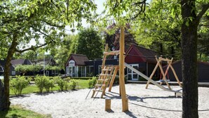 A playground with a wooden swing set and a slide, surrounded by sand and greenery. - 4-persoons bos by Interhome (Dalfsen)