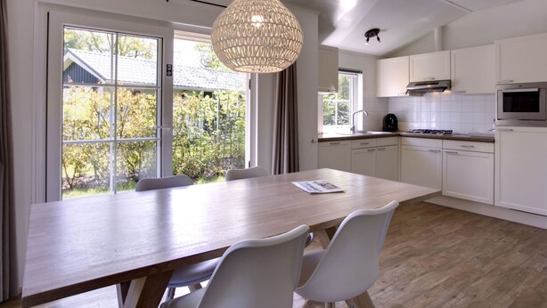 A modern kitchen with white cabinets, a wooden dining table, and a hanging light fixture. - 4-persoons bos by Interhome (Dalfsen)