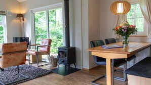 A modern living room with a large wooden table, leather chairs, a black wood-burning stove, and a large window with curtains. - 4-persoons bos by Interhome (Dalfsen)