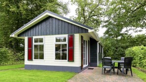 A small, single-story house with a dark roof and white siding, featuring a front porch with a brick pathway and two chairs. - 4-persoons bos by Interhome (Dalfsen)