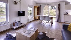 A modern living room with a television, a dining table with chairs, a kitchen area, and large windows. - 4-persoons bos by Interhome (Dalfsen)