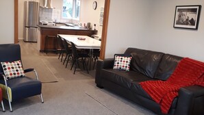 A living room with a black leather sofa, a blue armchair, and a wooden coffee table. There is a dining area with a white table and chairs, and a kitchen in the background. - Fairlie Family Home (Fairlie)