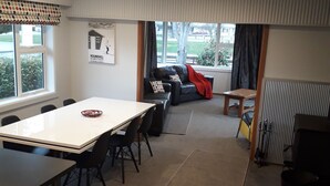 A modern, well-lit room with a dining table, chairs, a sofa, and a small table. There is a window with blinds, a radiator, and a poster on the wall. - Fairlie Family Home (Fairlie)