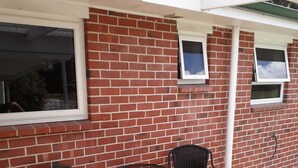 A patio with a brick wall, two wicker chairs, and a small round table. - Fairlie Family Home (Fairlie)