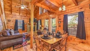 A wooden cabin interior with a dining table set for four, a leather sofa, and a fireplace. - Amazing Log Chalet, Scenic, Mountain View’s, Quiet (Sevierville)