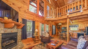 A cozy log cabin interior with a stone fireplace, a dining area, and a living room furnished with a leather sofa and a coffee table. - Amazing Log Chalet, Scenic, Mountain View’s, Quiet (Sevierville)