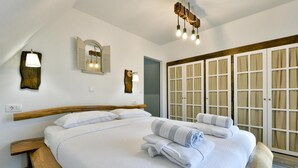 Een net opgemaakt bed met witte lakens en handdoeken, een houten hoofdbord en een groot raam met gordijnen.
