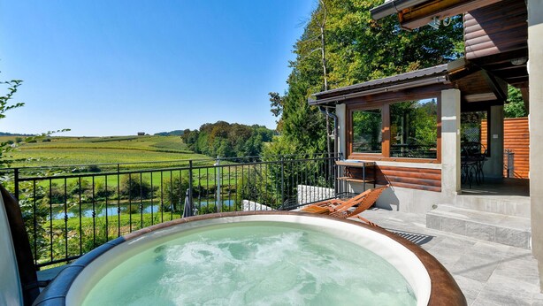 Een hottub met uitzicht op een rivier en velden, een houten terras en een overdekte zithoek met uitzicht op het landschap.