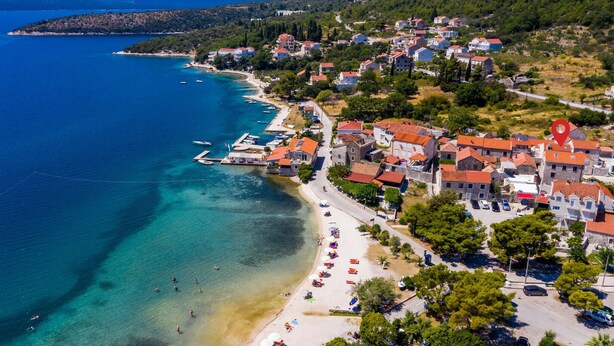 Vista aérea de un pueblo costero con playa, aguas azul turquesa y una mezcla de edificios residenciales.