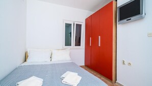 Un dormitorio con una cama, dos almohadas, un armario rojo, un televisor montado en la pared y una ventana.