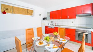 Una cocina moderna con armarios rojos, una mesa de comedor de vidrio y sillas naranjas.