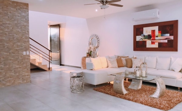 A modern living room with a white sofa, a glass coffee table, and a decorative mirror.
