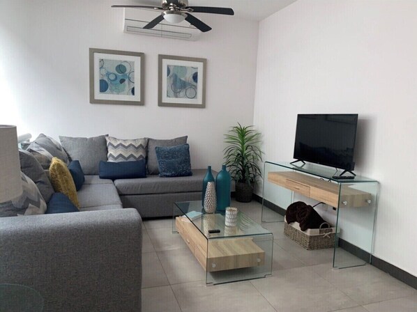 Un salon moderne avec un canapé gris, une table basse en verre et un téléviseur posé sur un meuble en verre.