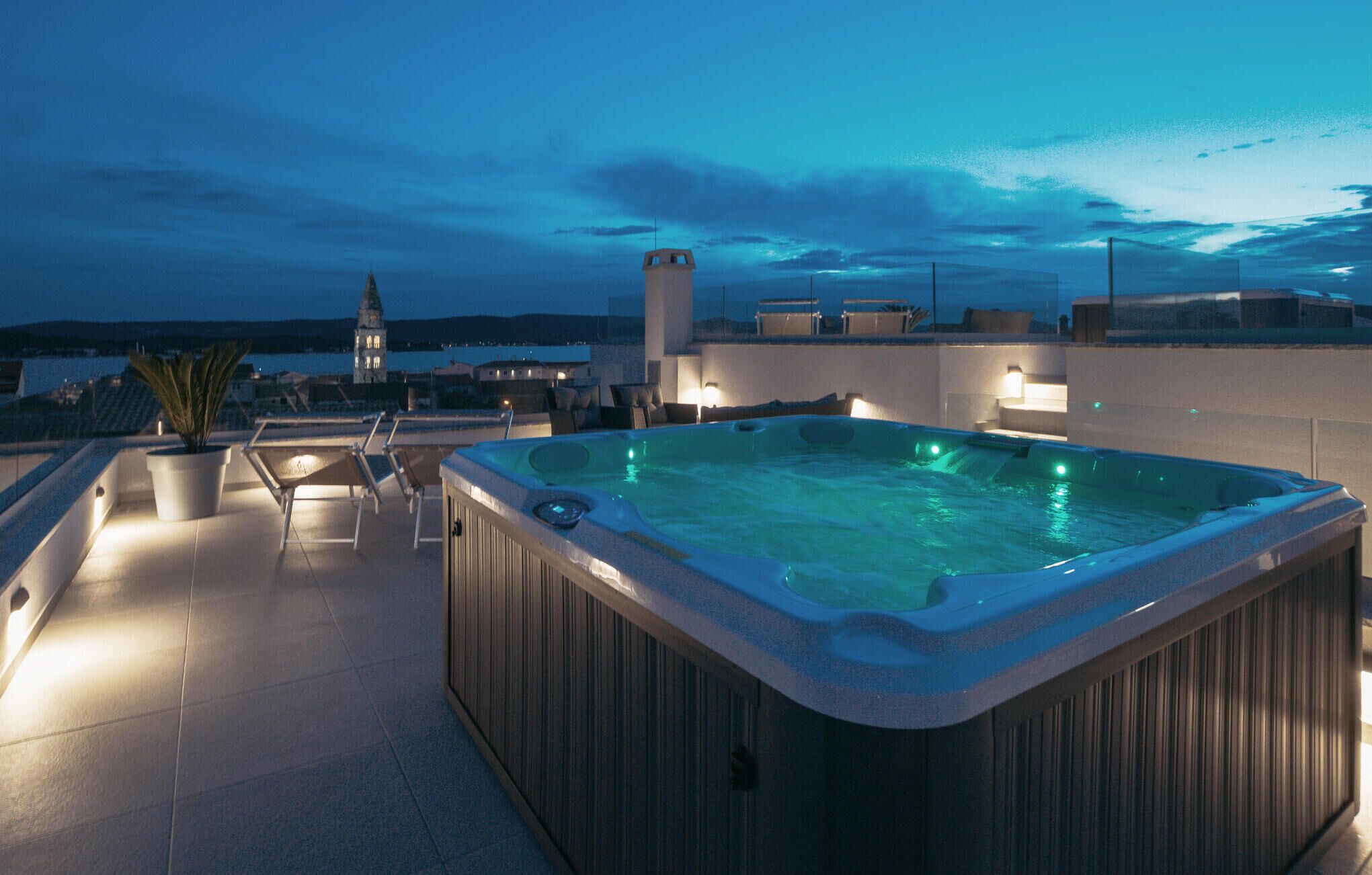 Terraza en la azotea con un jacuzzi, sillas de descanso y vista a una torre distante.
