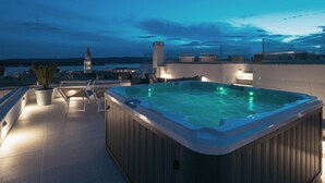 Eine Dachterrasse mit Whirlpool, Liegestühlen und Blick auf einen entfernten Turm.