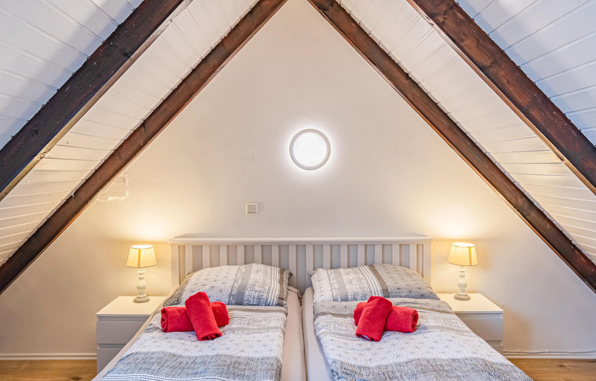 Ein Schlafzimmer mit zwei Betten, jeweils mit einem roten Handtuch, unter einer schrägen Decke mit Holzbalken.