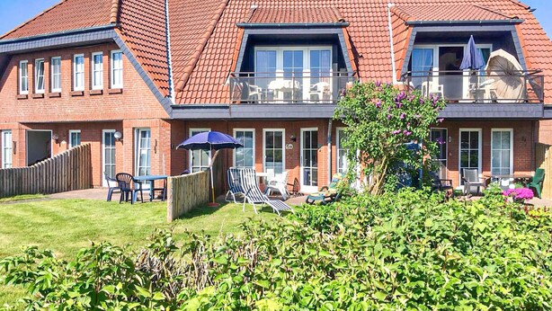 Ein zweistöckiges Gebäude mit rotem Ziegeldach, einem Balkon mit Gartenmöbeln und einem gepflegten Garten.