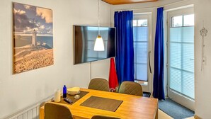 Ein Konferenzraum mit einem Holztisch, vier Stühlen, einem Fernseher und einem Gemälde eines Leuchtturms.